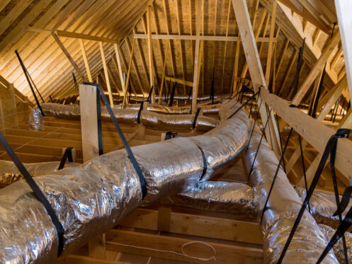 In a newly built home under construction, ventilation pipes are found in the silver insulation material on the ceiling of the attic
